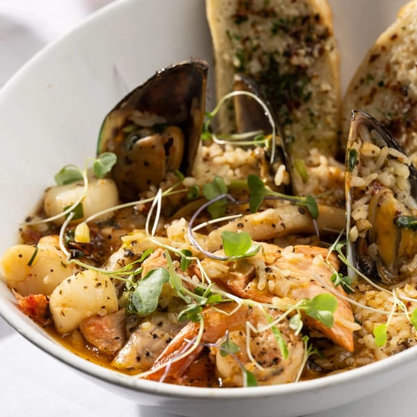 A Primavera Ristorante seafood risotto with mussels, scallops, shrimp, and garlic bread in a white bowl.