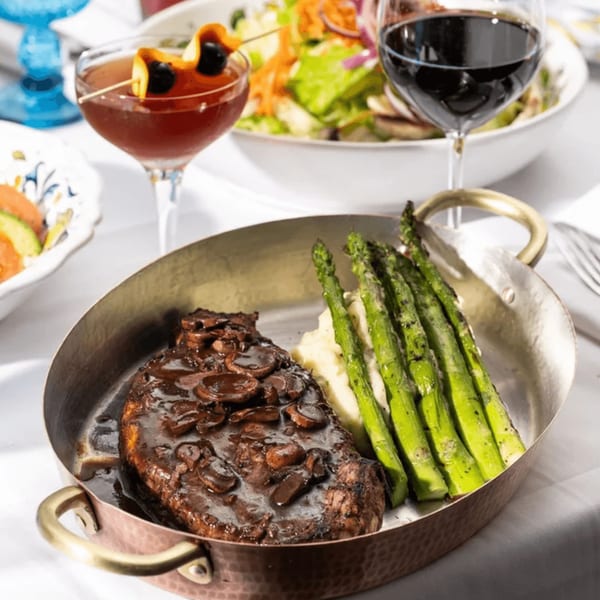 Primavera Ristorante's steak with mushroom sauce, mashed potatoes, and asparagus, with cocktails and salad.