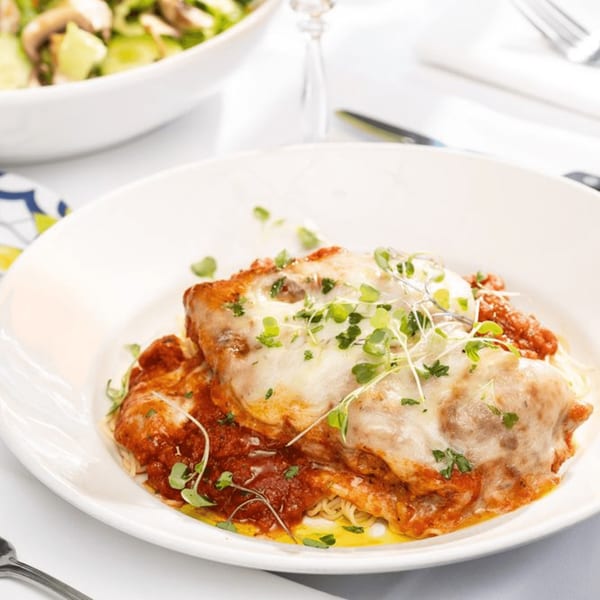 Chicken parmesan with melted mozzarella, red sauce, and microgreens, served with spaghetti.